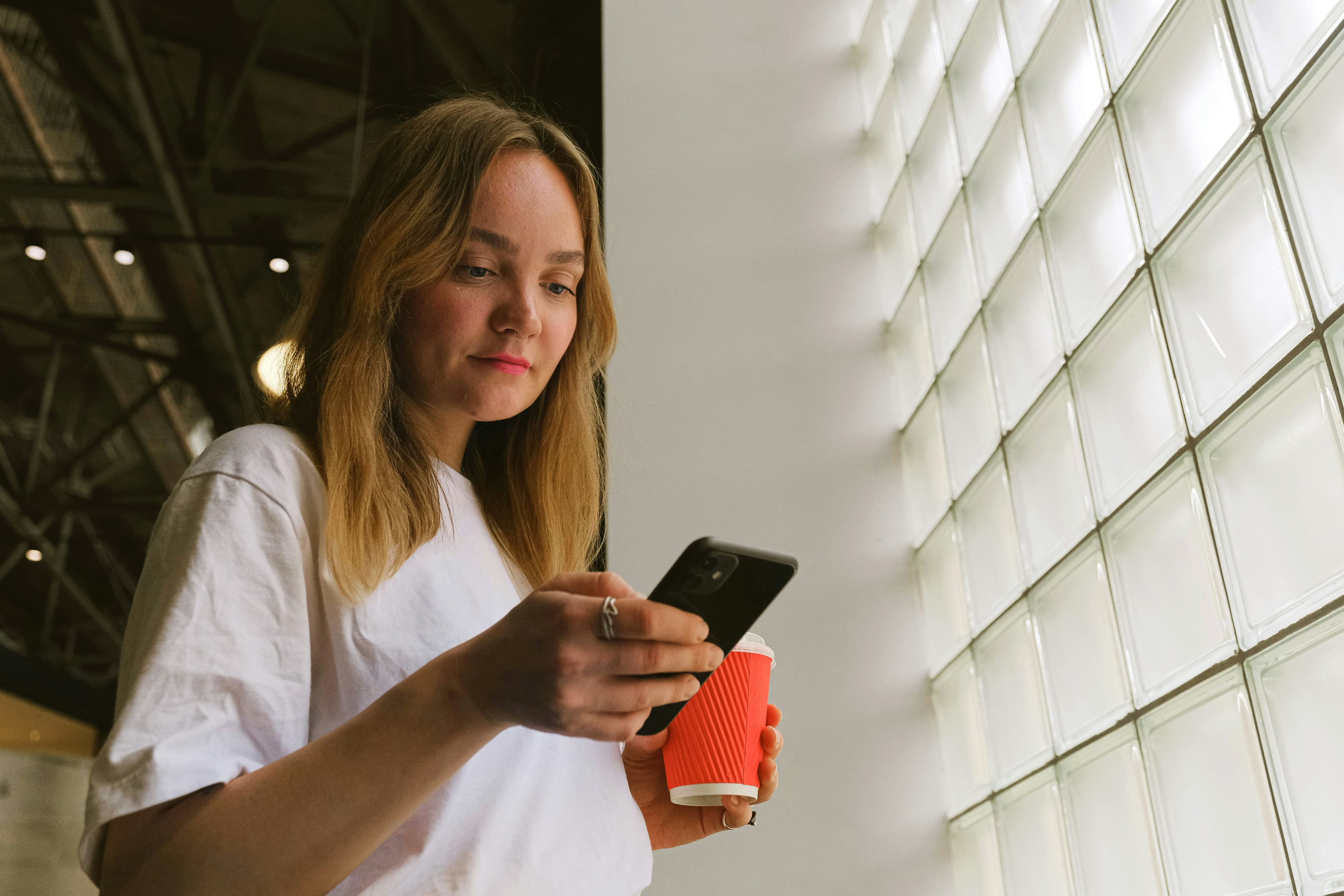Donna che usa Satispay dallo smarphone, una tazza di caffé in mano